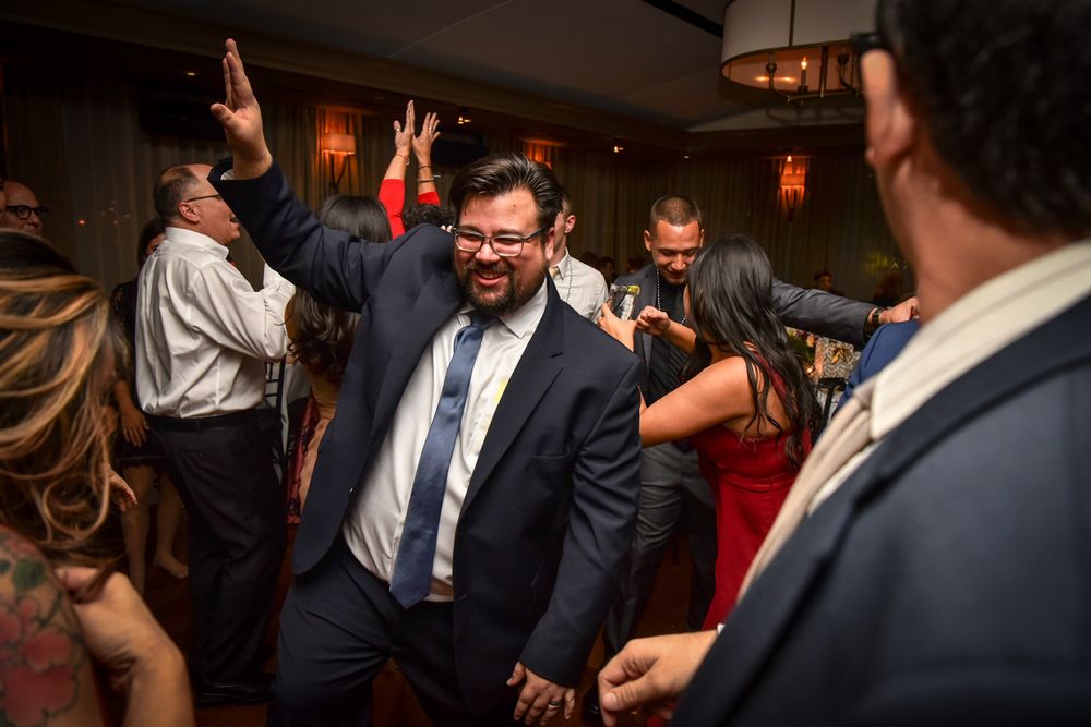 Wedding guests dancing and celebrating on a dimly lit dance floor at an indoor reception party.