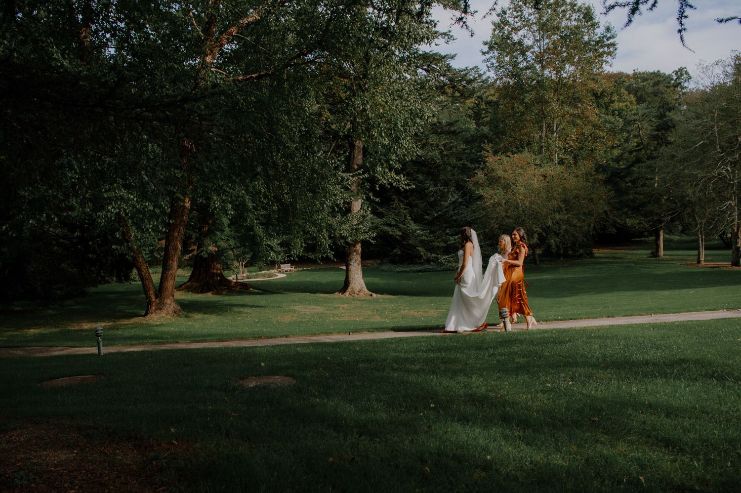 People in formal attire celebrate a wedding outdoors at a sunny outdoor reception venue in a wooded setting.