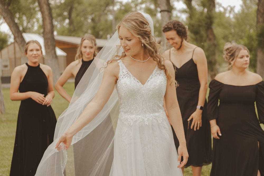 A bride in a white gown celebrates with bridesmaids wearing black dresses outdoors.