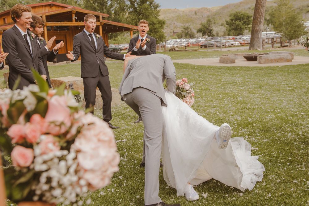 A wedding party poses for photos on a grassy lawn with mountains in the background.