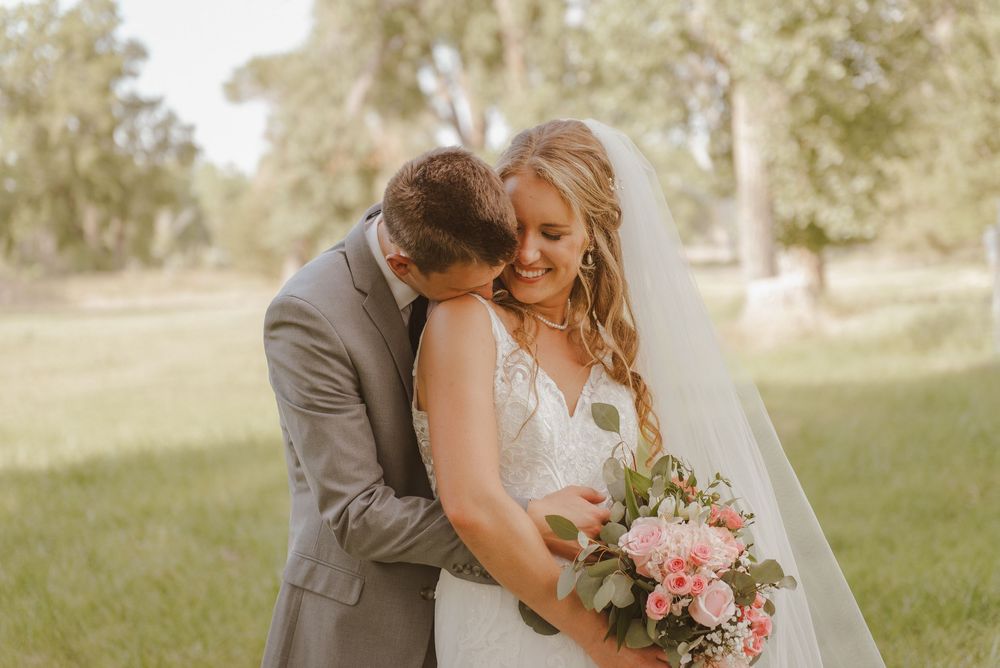Tender wedding moments photographed in a sun-drenched meadow with pink bouquet details.