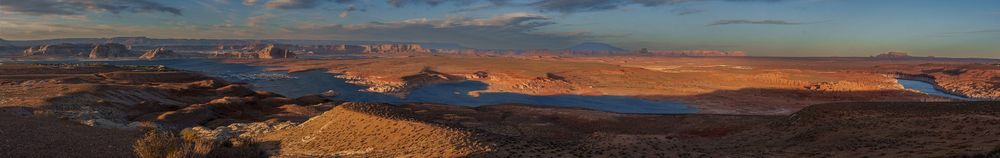 A panoramic desert vista shows rugged red rock formations and distant mountains under a vibrant sunset sky near Page, Arizona.