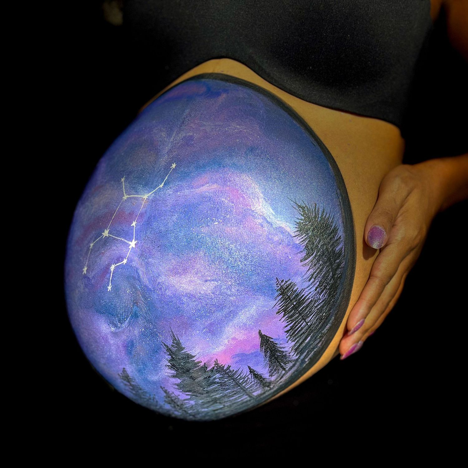 Belly painted with a galaxy scene with purple and blue colors on a dark background.