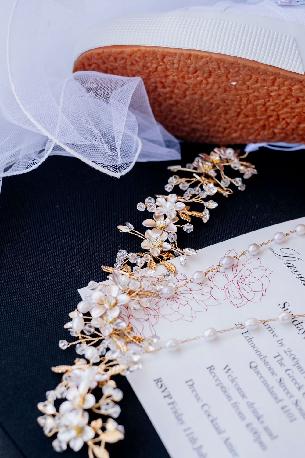 Delicate floral bridal headpiece with gold and pearl details lies on wedding invitation card.