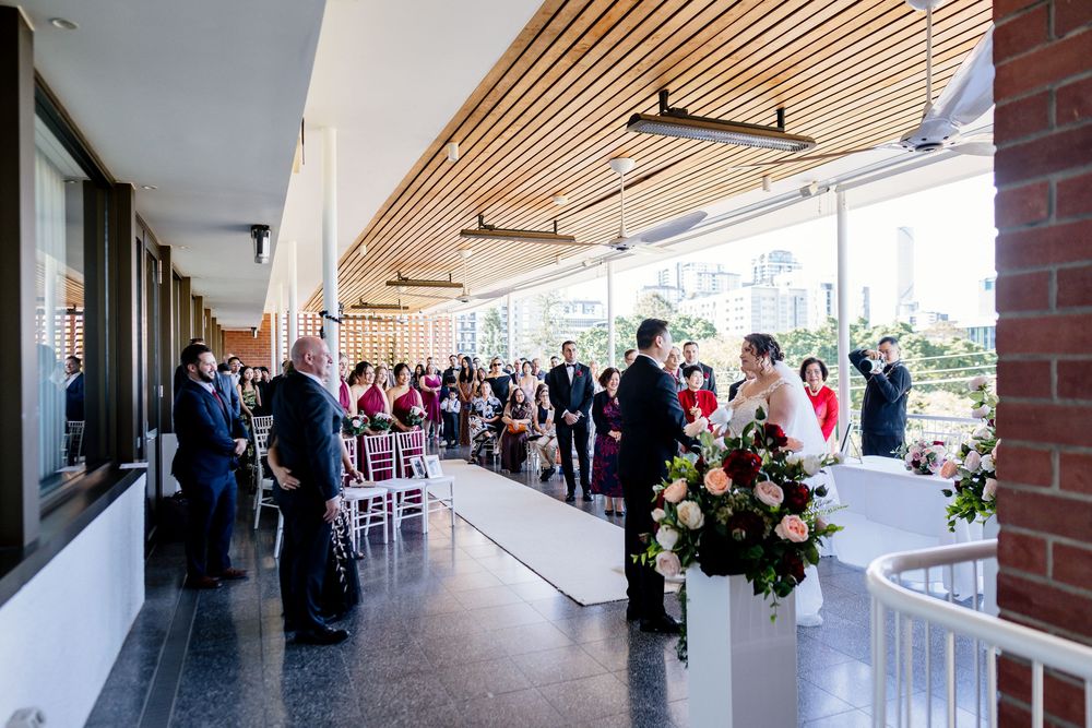 Panoramic view of a modern building interior with wooden slat ceiling and brick columns along a covered walkway.