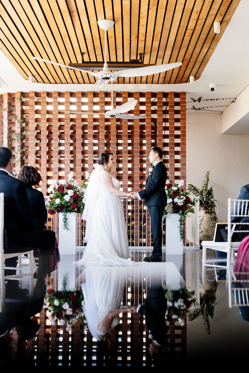 Wedding ceremony setup in modern venue with wood slat wall dividers and floral arrangements.