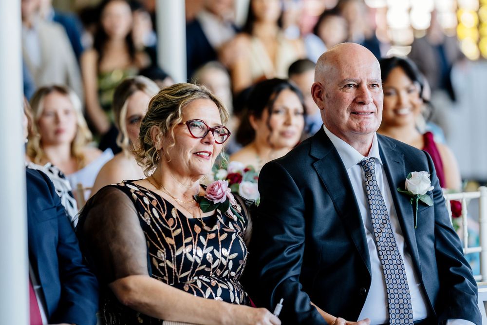 Wedding guests seated in rows watch ceremony with joyful expressions in bright indoor venue.