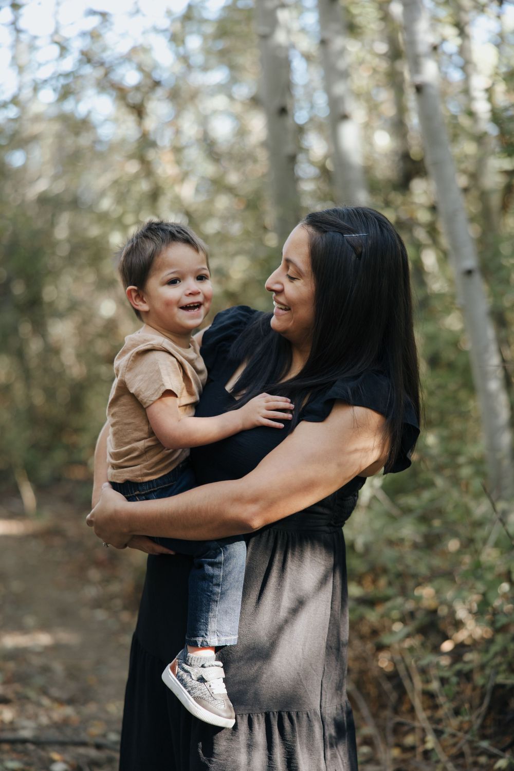 Candid outdoor photoshoot showing playful moments between parent and child in a wooded setting.