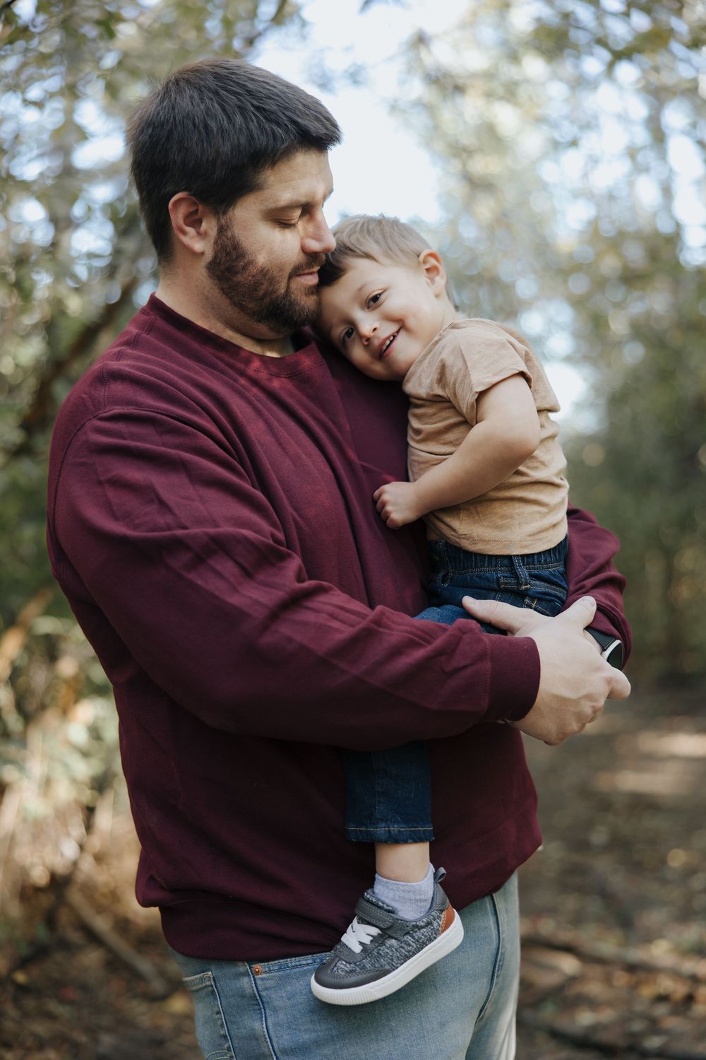 Parent and child sharing joyful moments in burgundy sweater against natural forest backdrop.