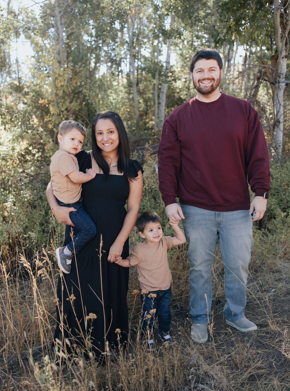 Family portrait in casual attire standing together in natural outdoor setting.