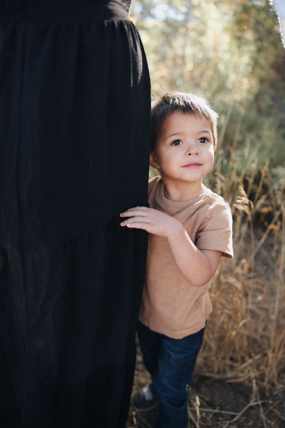 Young child in tan shirt reaching out during outdoor photo session.