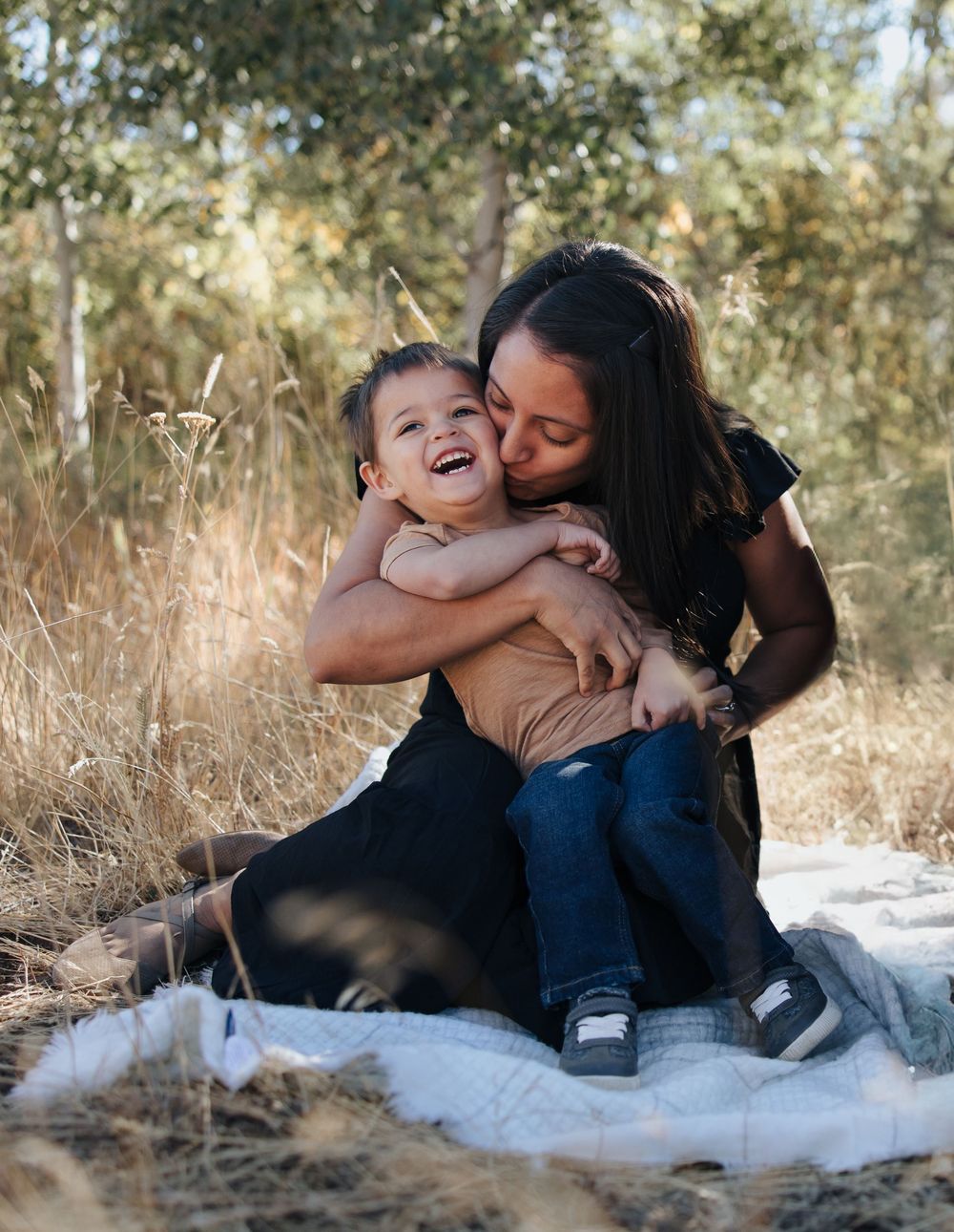A heartwarming family moment captured on a white blanket surrounded by tall grass.