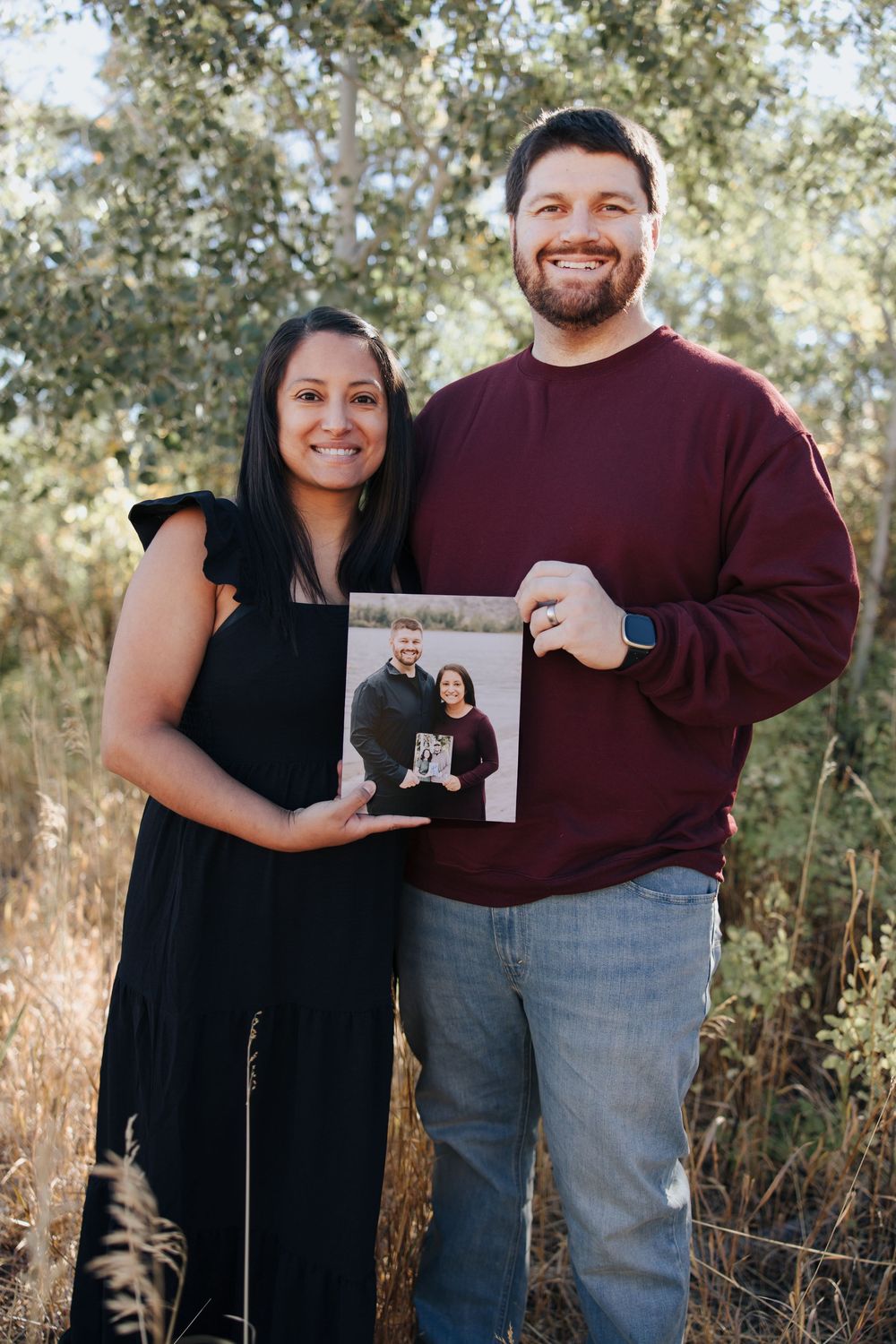 Couple holding photo prints during outdoor portrait session in natural setting.