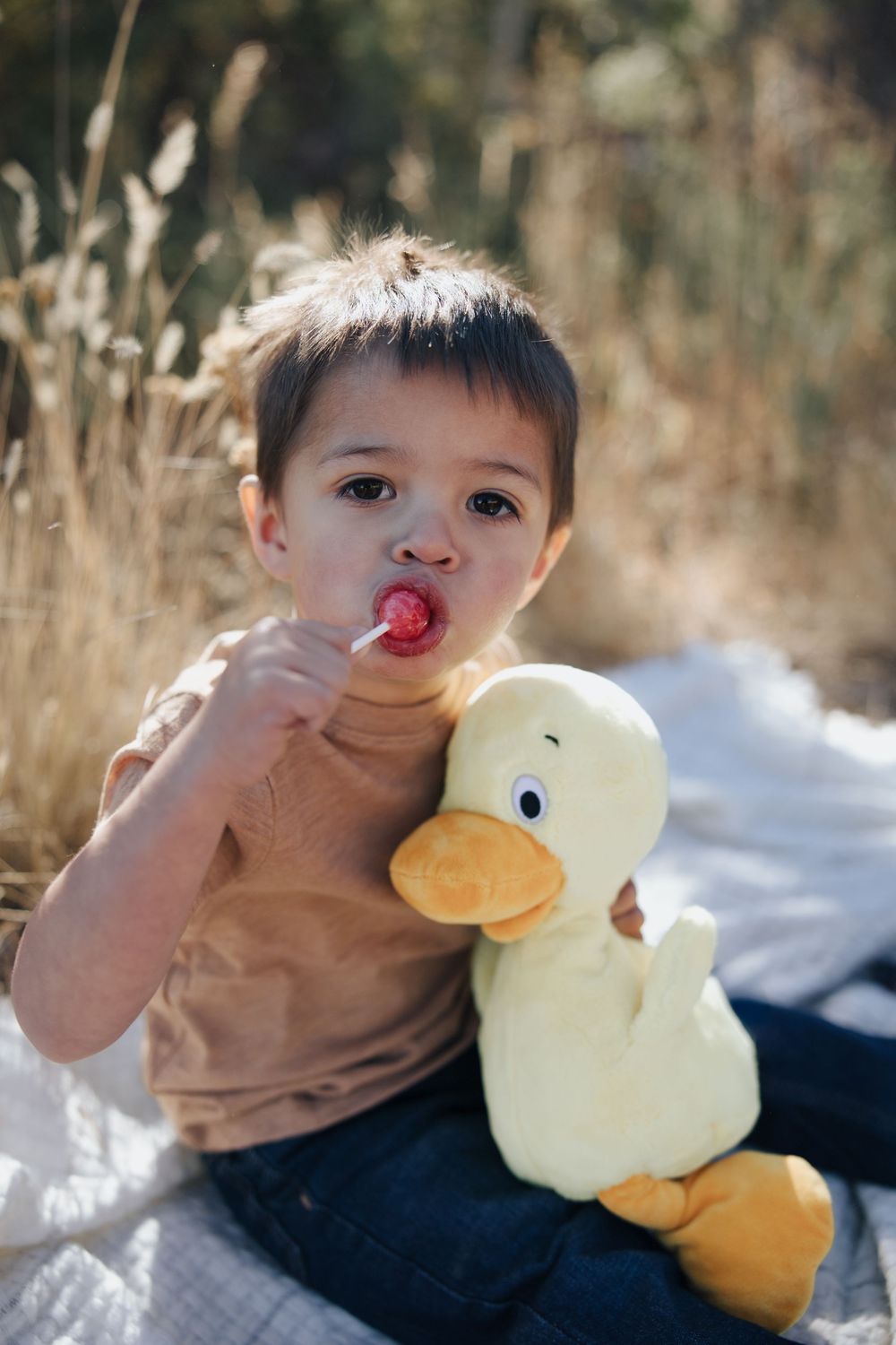 A child plays with a plush yellow duck toy while lying on a blanket in the snow.