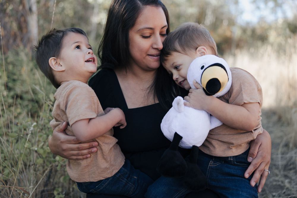 A tender family moment captured outdoors with a plush toy and natural backdrop.