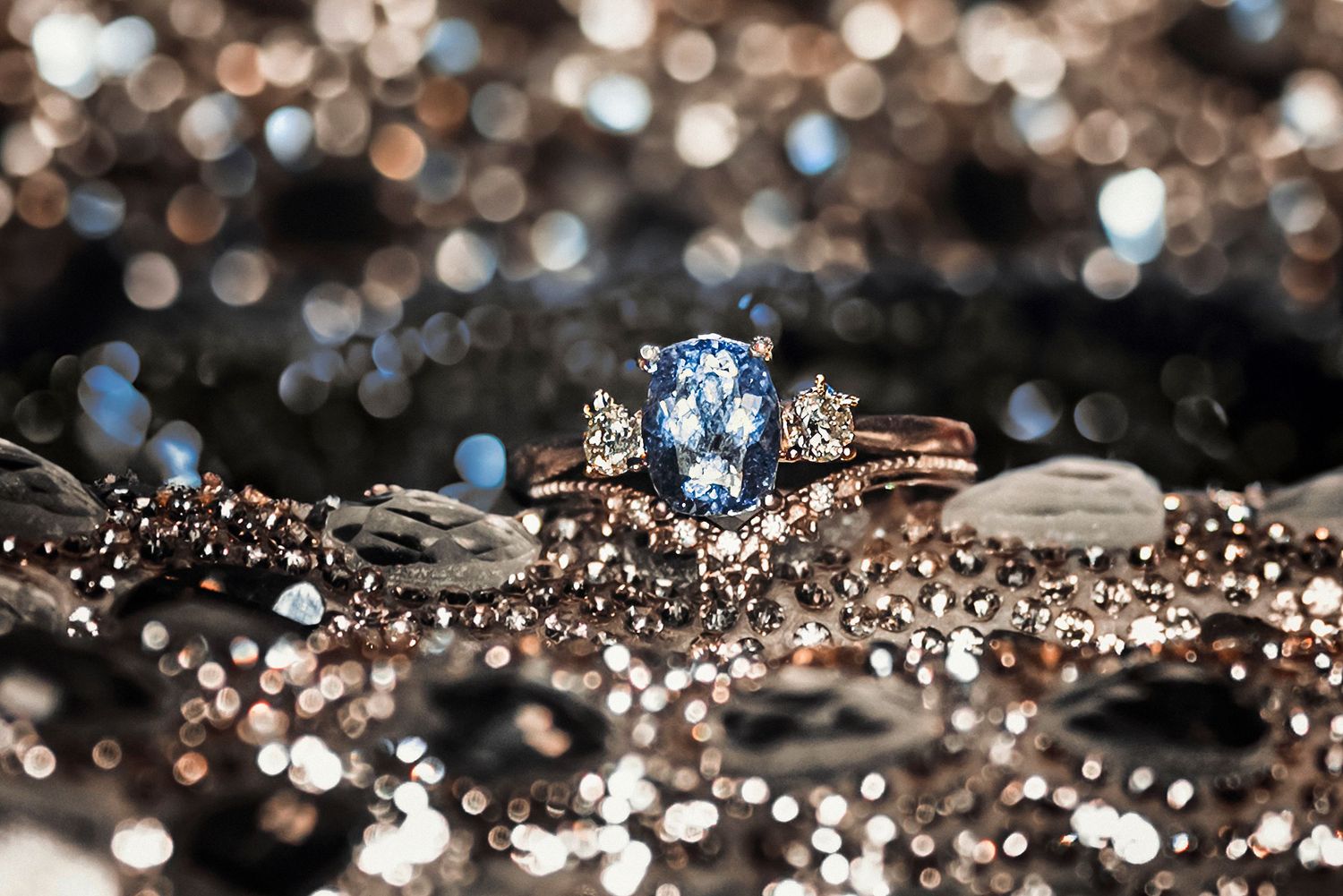 Blue sapphire diamond engagement ring with matching band on sparkling silver bokeh background.