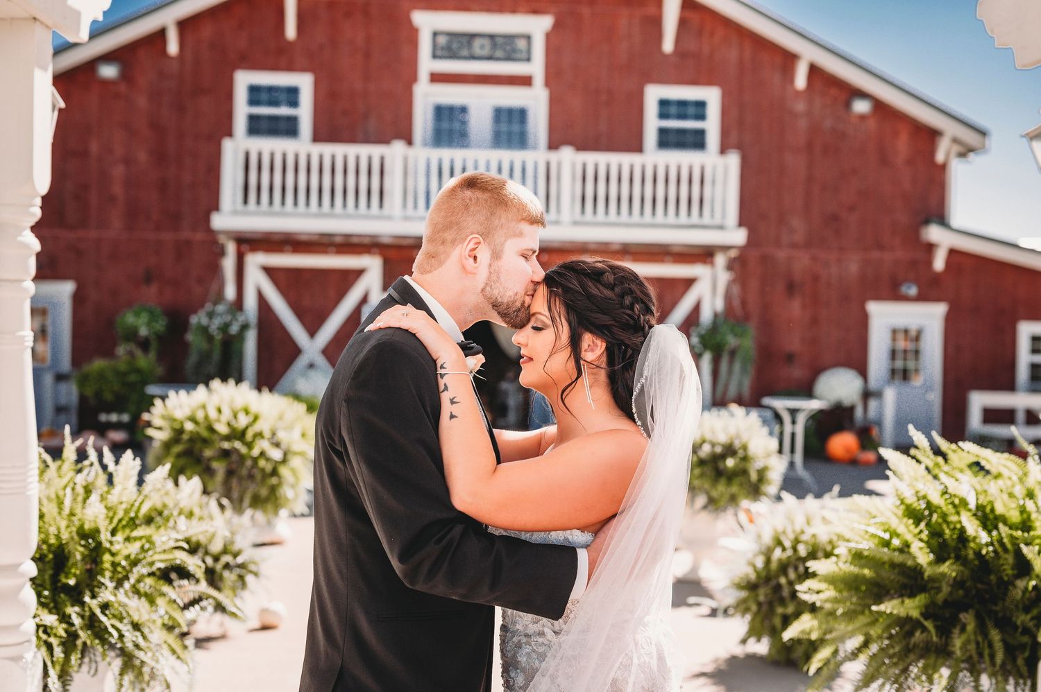Bride and groom share tender forehead touch moment outside classic red barn wedding venue. Bessie's Barn