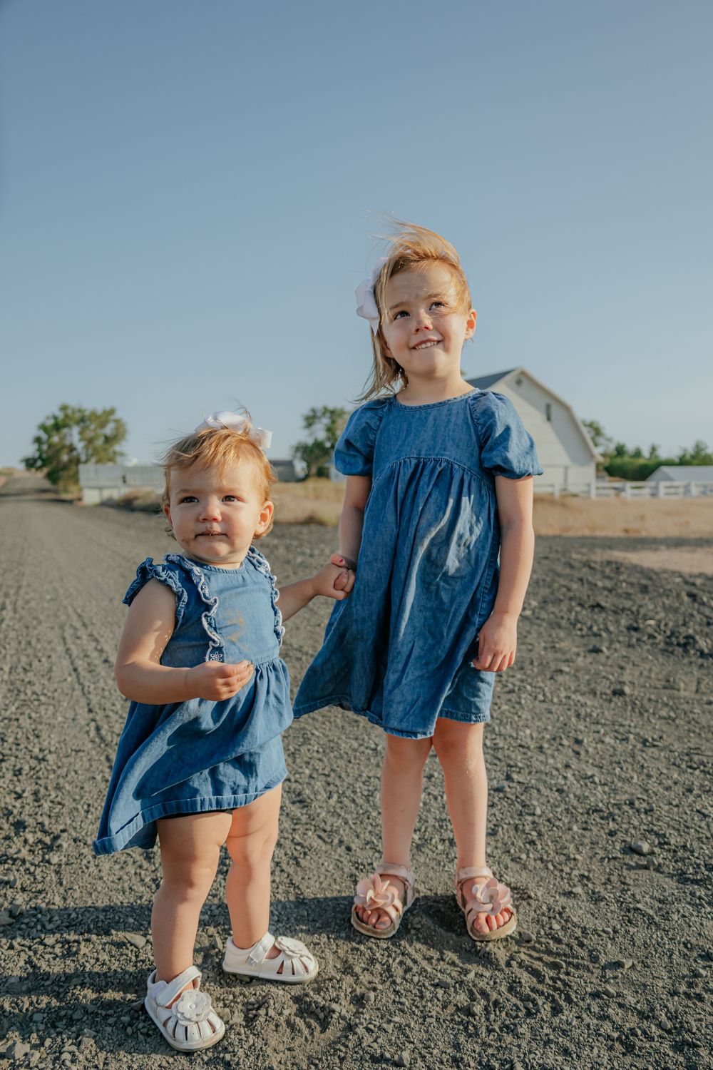 Two children in matching denim outfits playing on rocky ground against a blue sky.