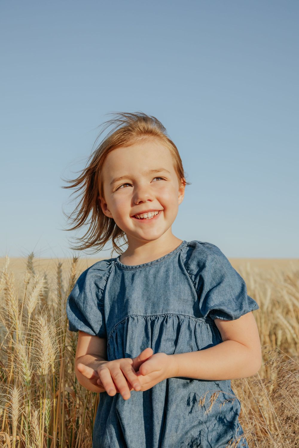 Child in blue dress playing joyfully in a wheat field during sunset.