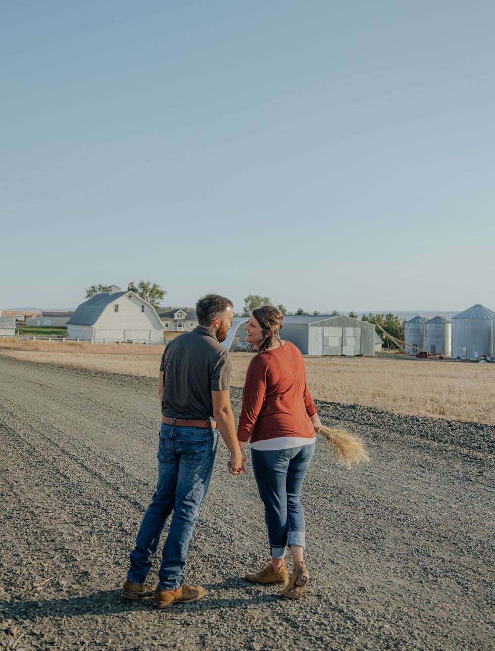 Family walking together on rocky terrain with farm buildings in background.