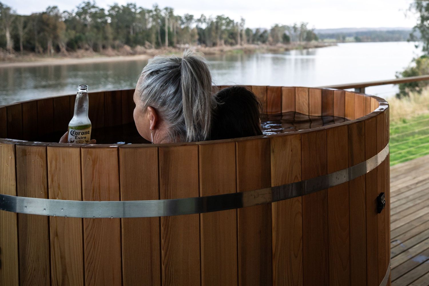 Four people relax in a wooden hot tub surrounded by outdoor scenery and trees.