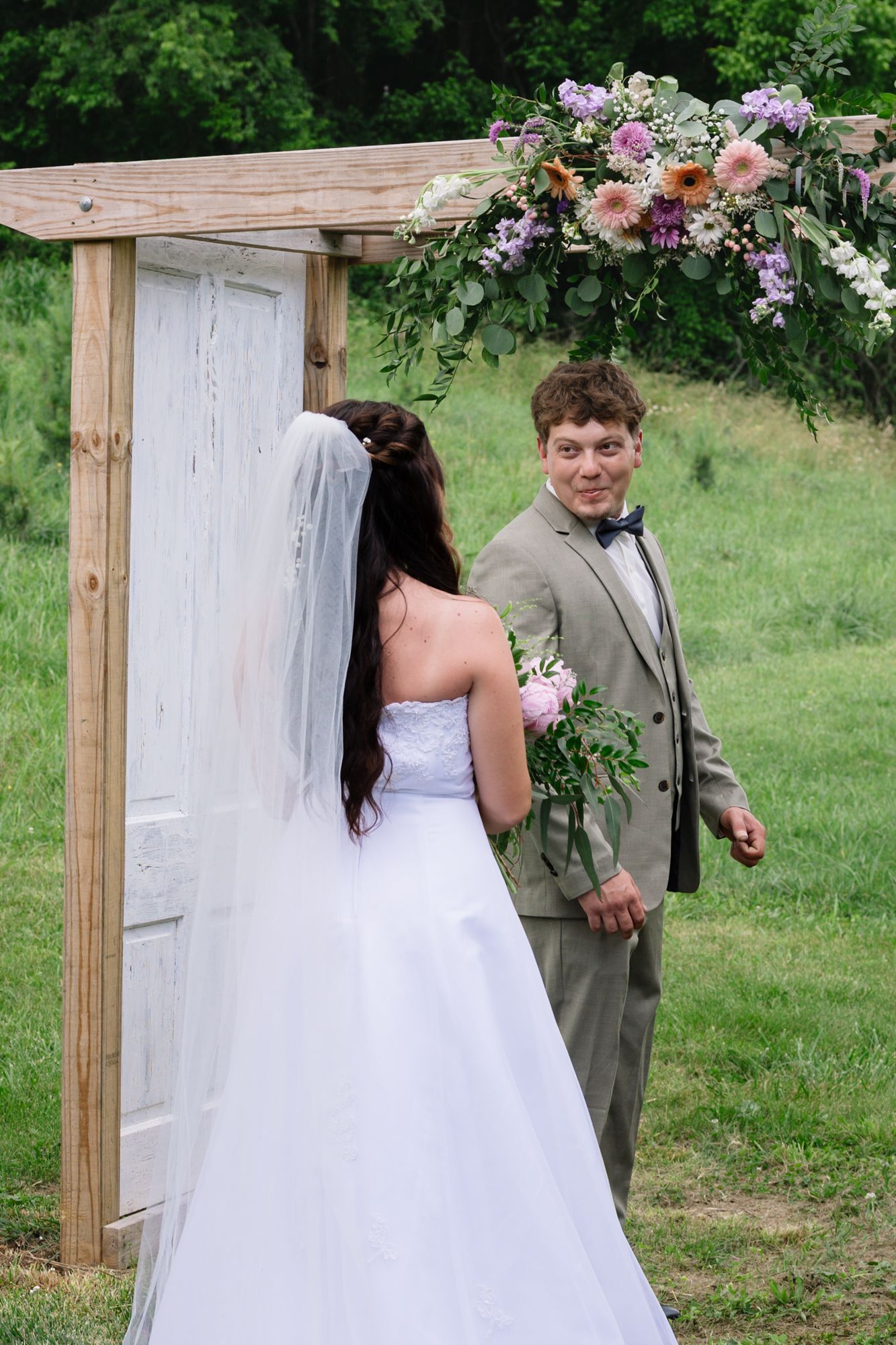 Creative wedding photoshoot setup featuring a freestanding white door frame in an outdoor garden setting.