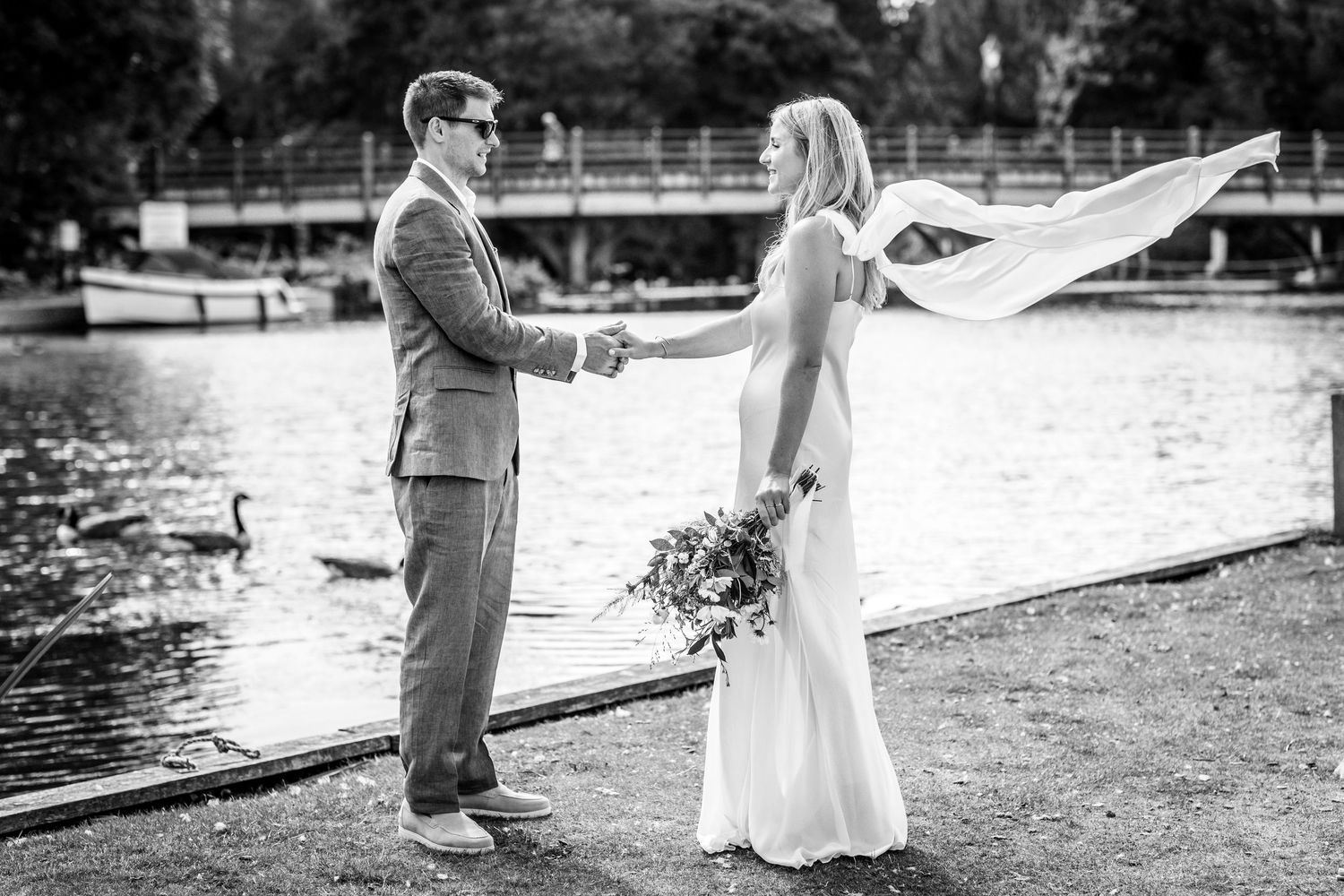 Black and white wedding photo by a lake with swans in the background.