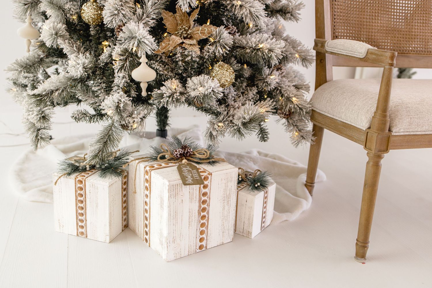A rustic holiday gift wrapped in white paper with pine branches, pinecones, and gold ribbon decorations.