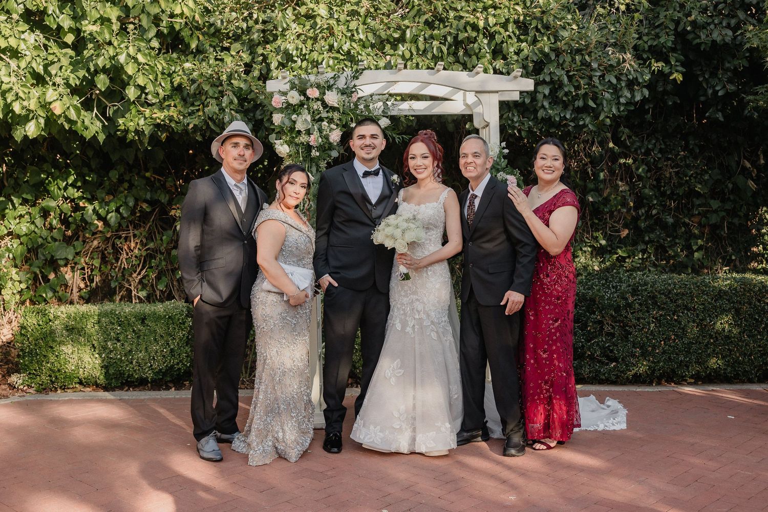 Wedding party poses together on a green lawn with pink floral arrangements and trees in the background for Sacramento wedding