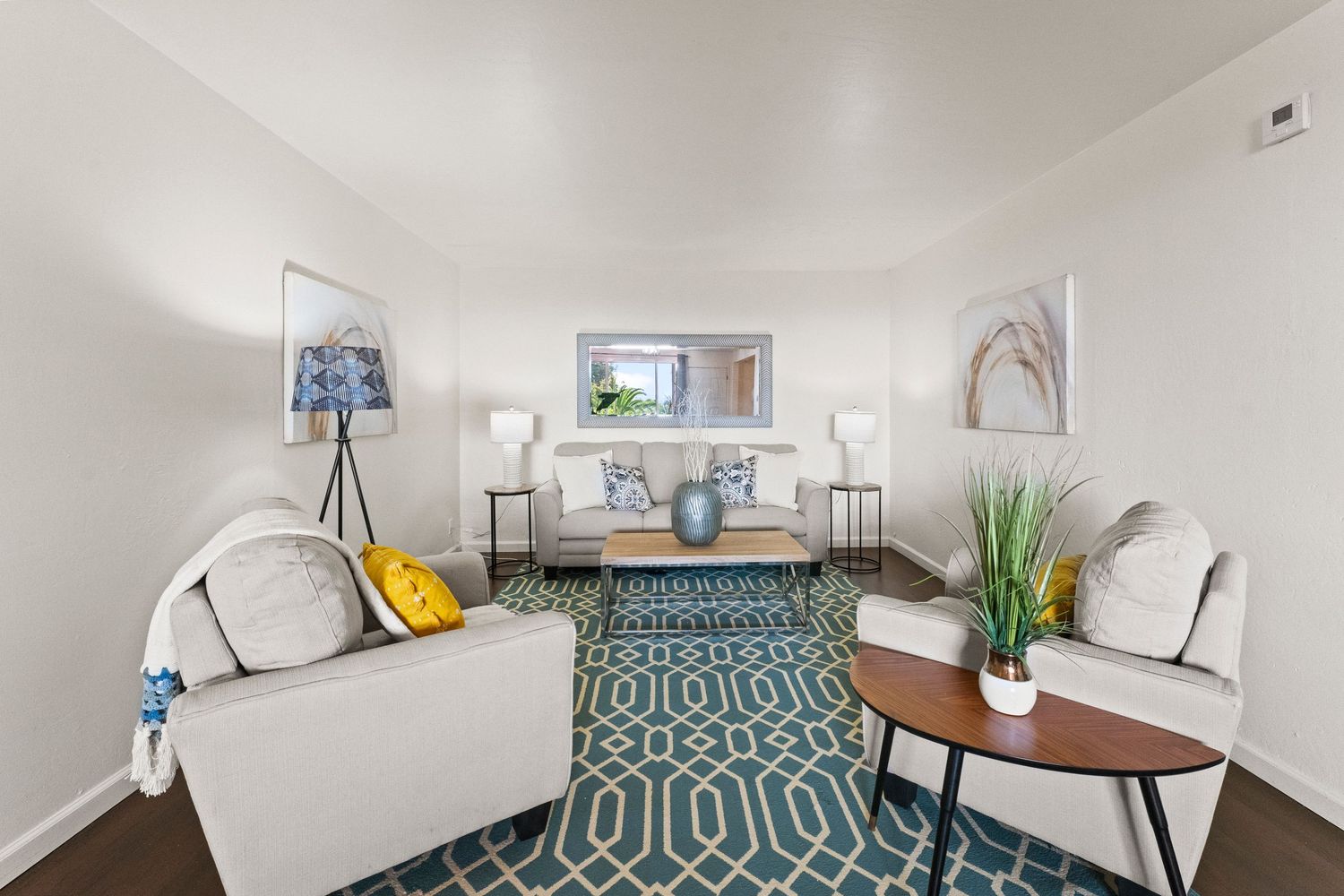 Modern apartment interior with white walls and geometric patterned rug showing multiple seating areas.