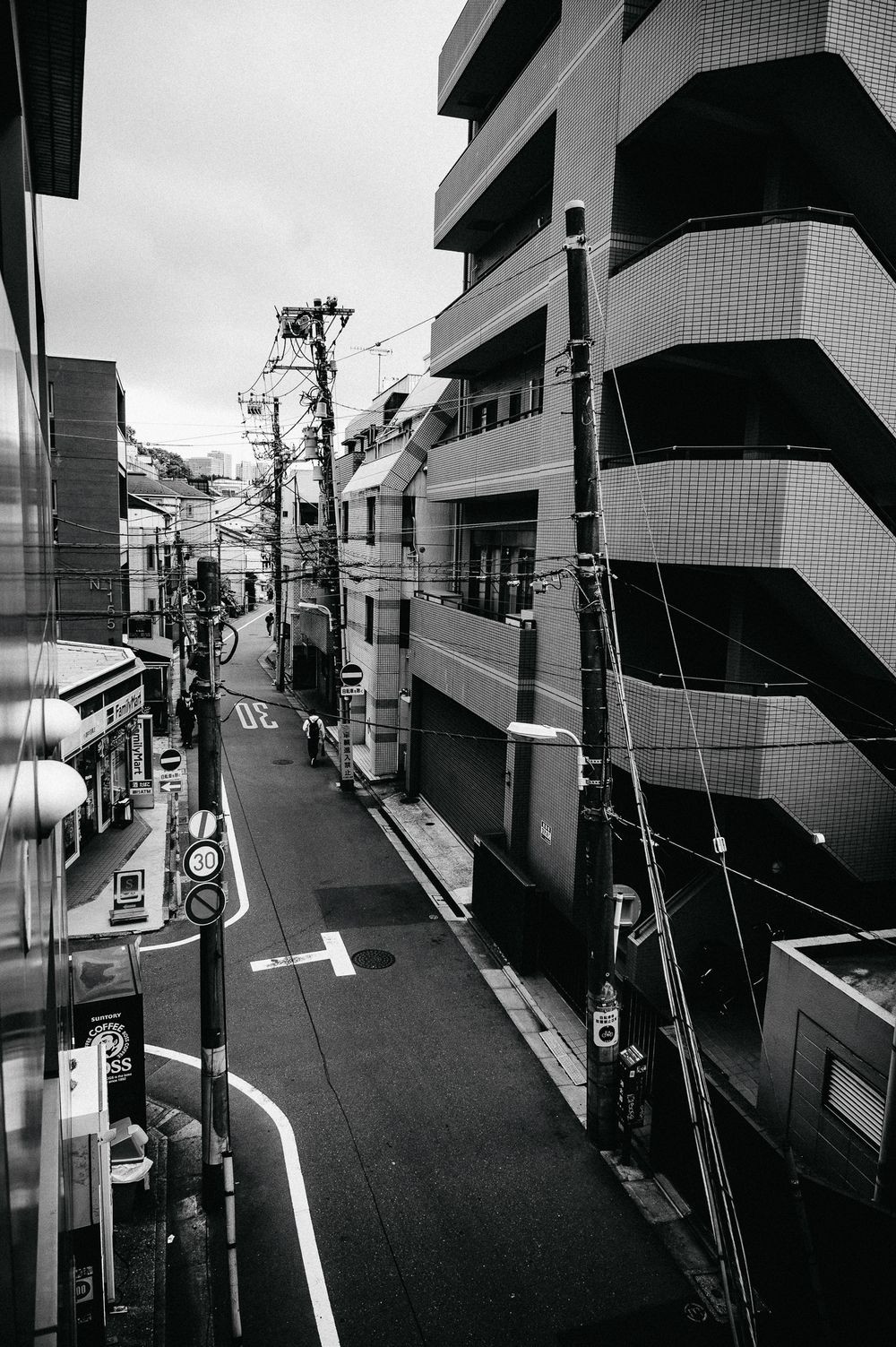 Black and white street view of modern Japanese residential buildings with curved architecture and utility poles in Tokyo.