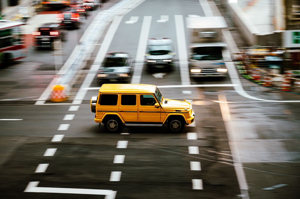 Cars and yellow taxi cabs move through wet city streets during rainy weather, creating reflective patterns on the road.