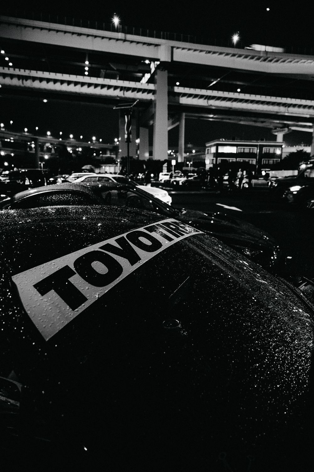 Wet black car surface showing FOX branding in monochromatic lighting at a parking structure.