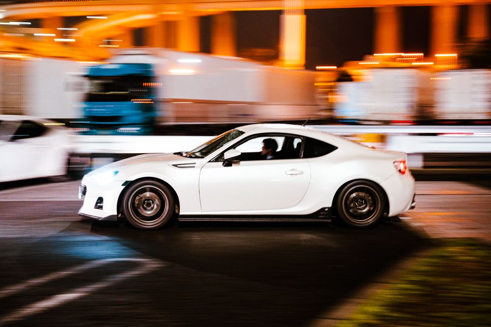 Motion-blurred white sports cars speeding past on a street with orange ambient lighting.