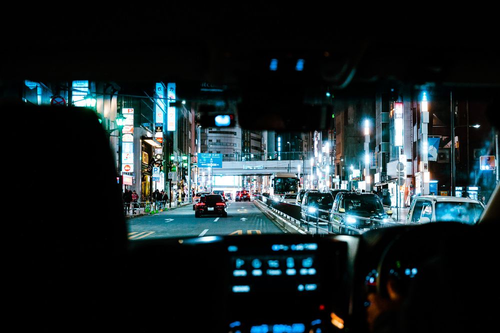 Dark urban street scene with neon blue reflections and lights illuminating a city street at night in moody atmosphere.