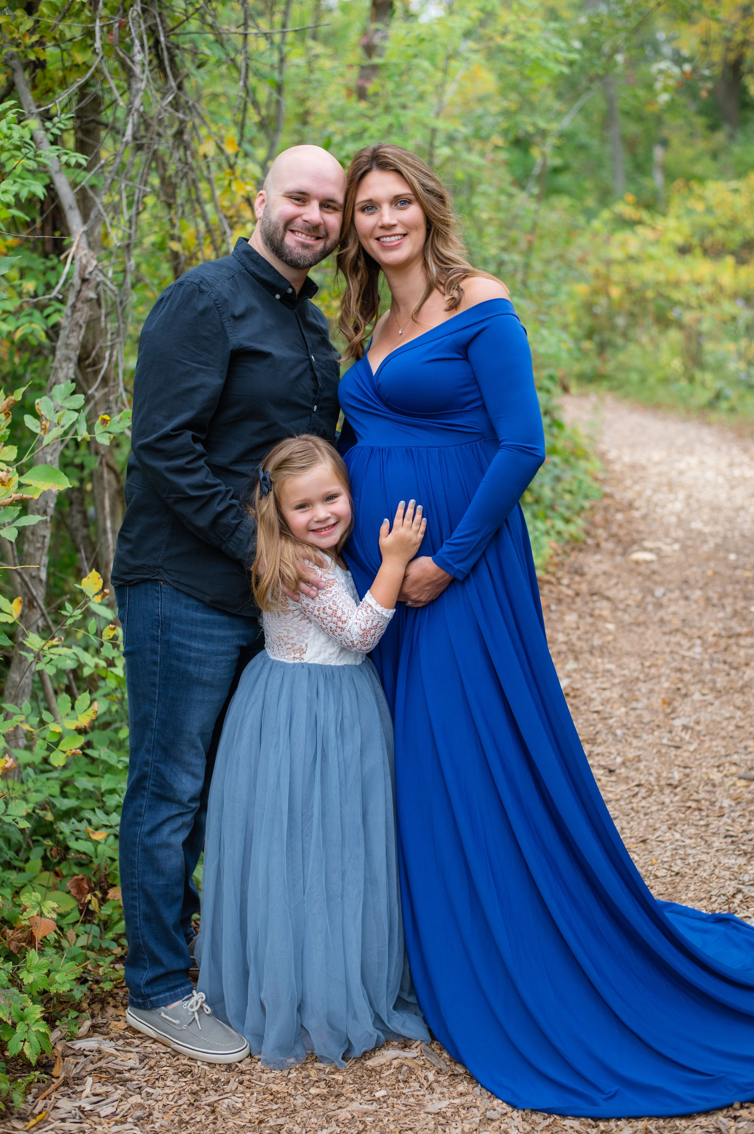 A family in coordinated outfits poses together along a wooded path during an autumn photo session.