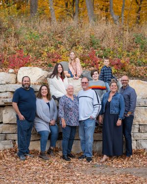A group relaxes casually against a stone wall during an autumn photoshoot with fallen leaves scattered around.