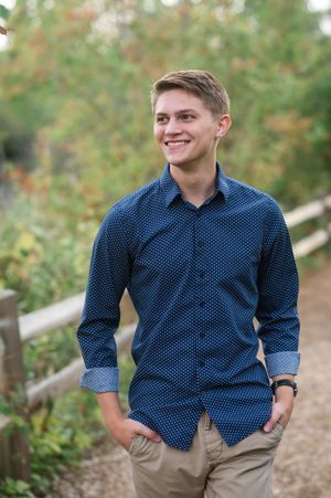 Casual outdoor portrait featuring a navy polka dot button-down shirt and khaki pants against a nature background.
