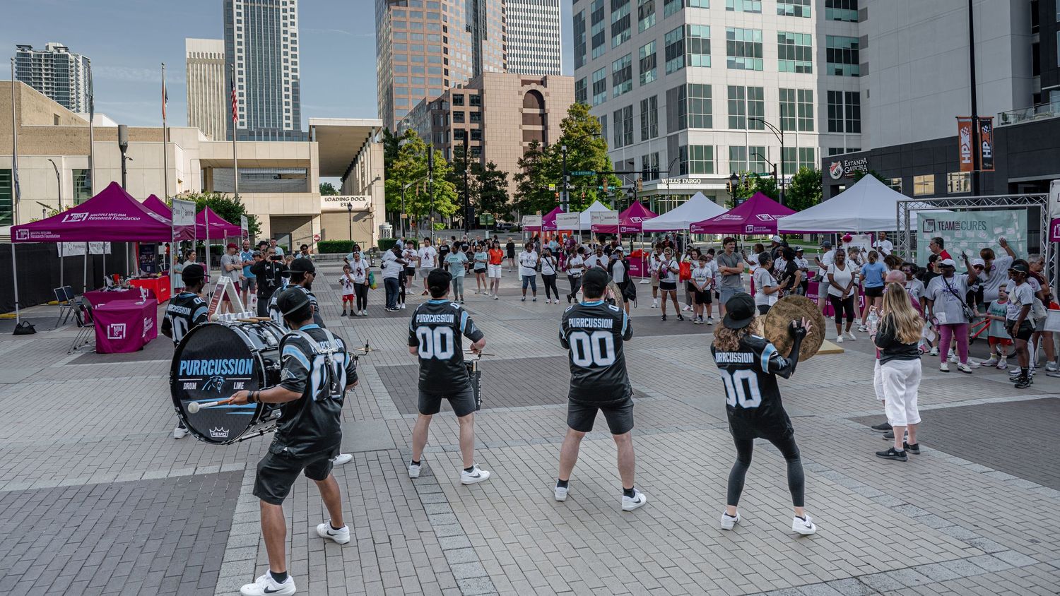A marching band performs for a crowd at an outdoor Multiple Myeloma Research Foundation charity walk event.