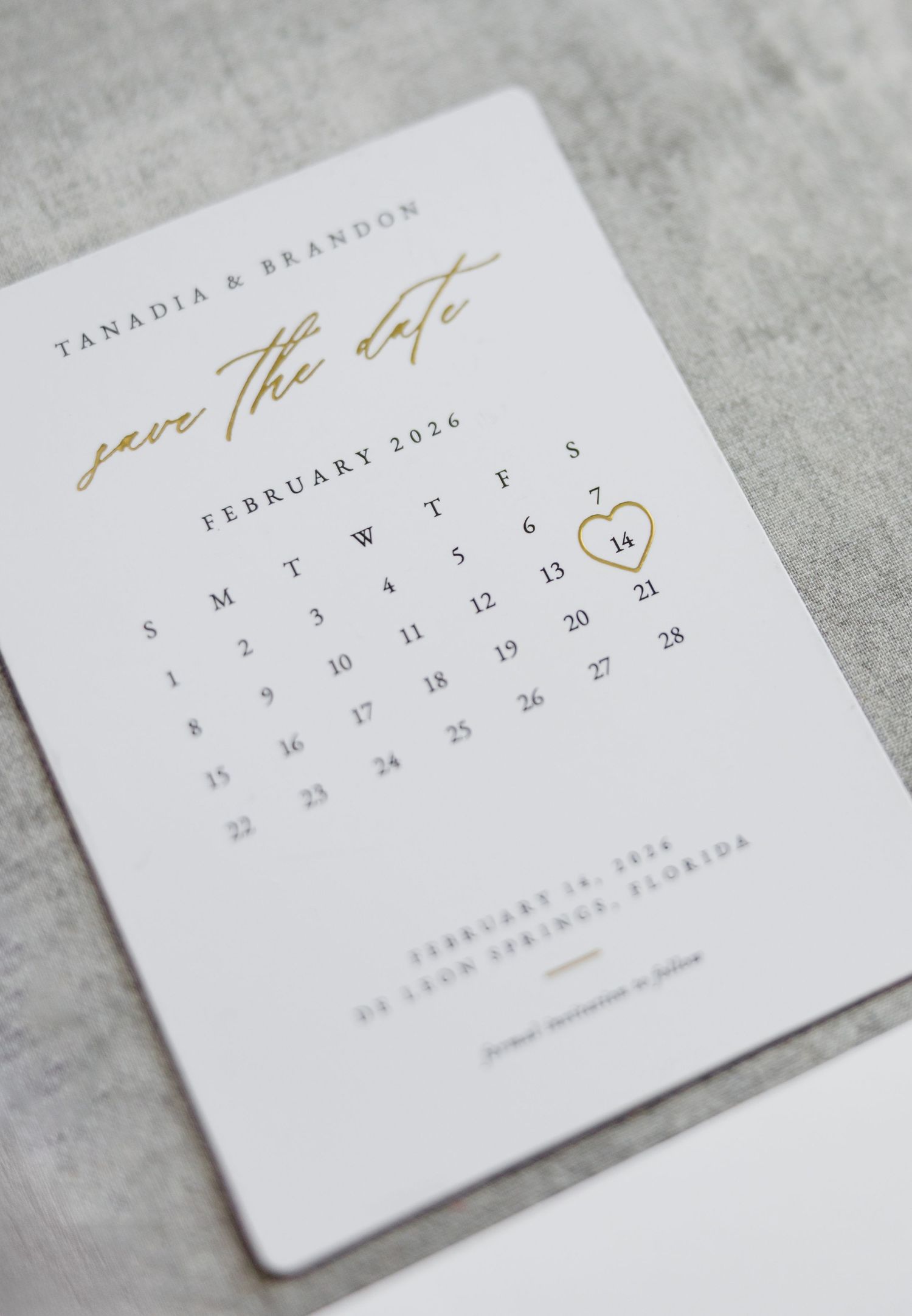 Gold foil save the date card for Tanadia and Brandon featuring a February 2026 calendar with heart on the 14th.