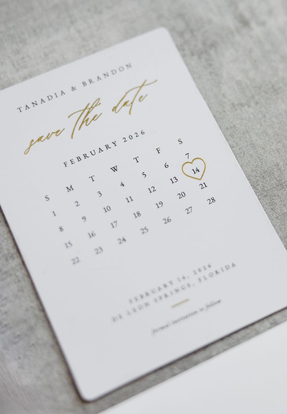Gold foil save the date card for Tanadia and Brandon featuring a February 2026 calendar with heart on the 14th.