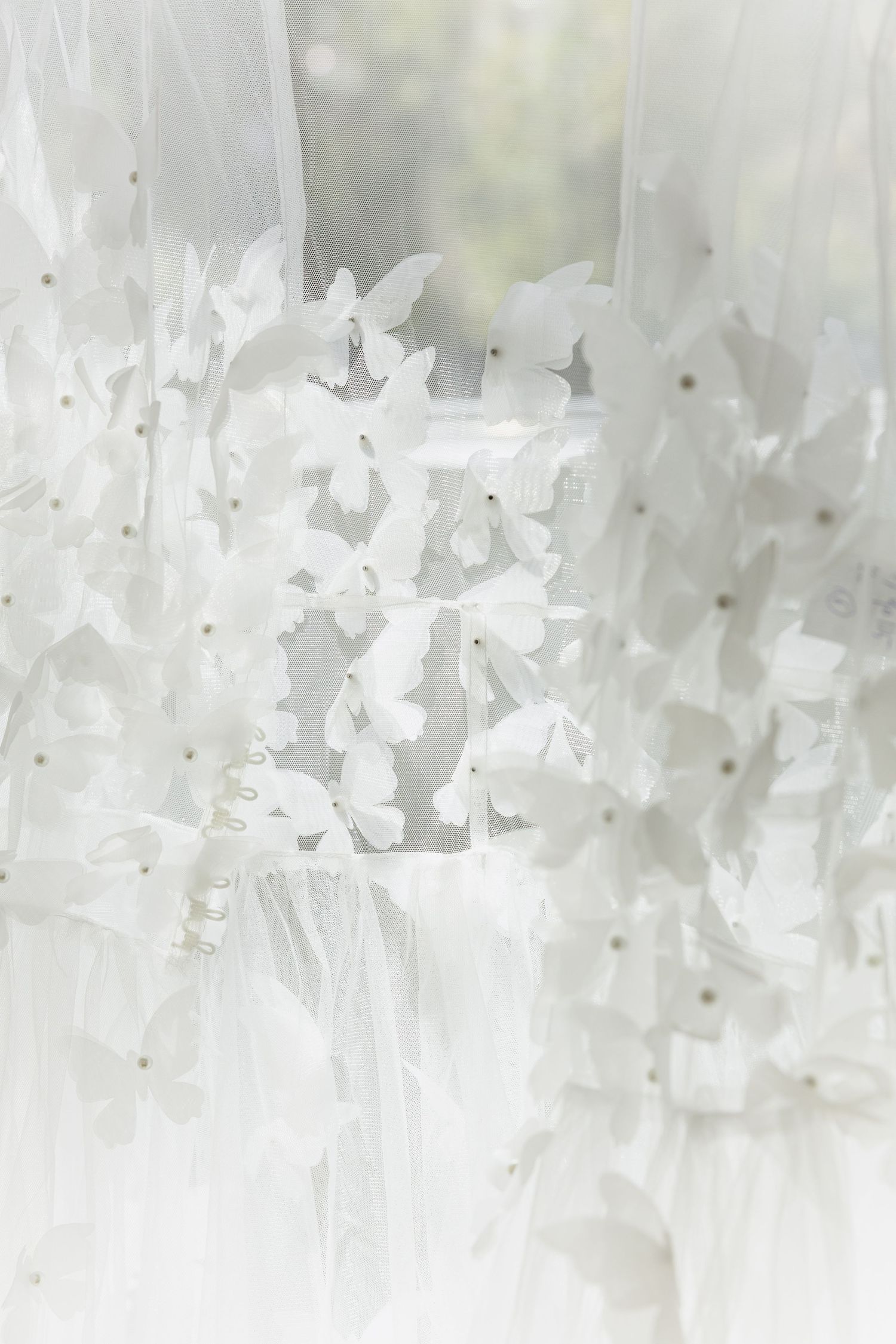 White wedding dress adorned with delicate butterfly appliques and pearl details on sheer tulle fabric.