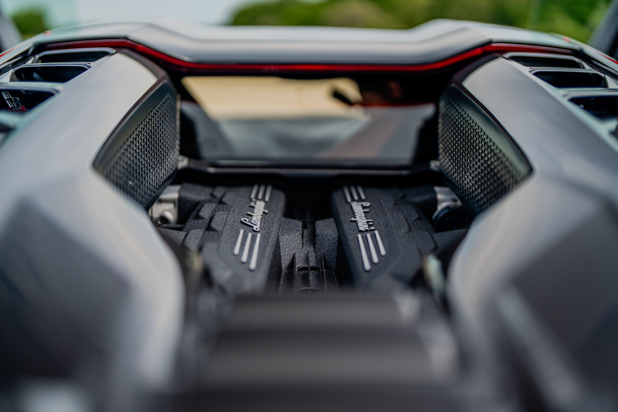 Close-up view of a high-performance Lamborghini V12 engine with carbon fiber details visible through open engine bay.