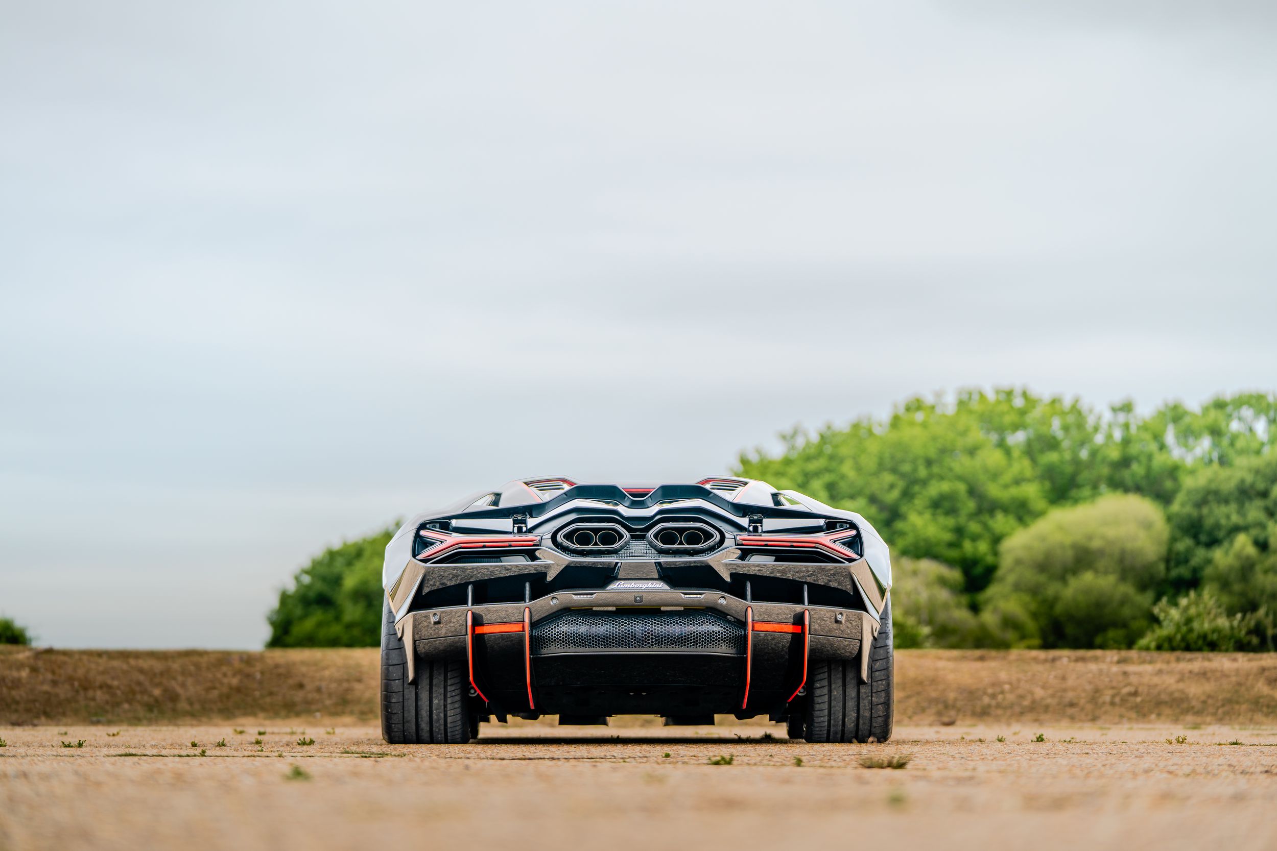 Rear view of a white Koenigsegg hypercar parked on a dirt road with trees in background.