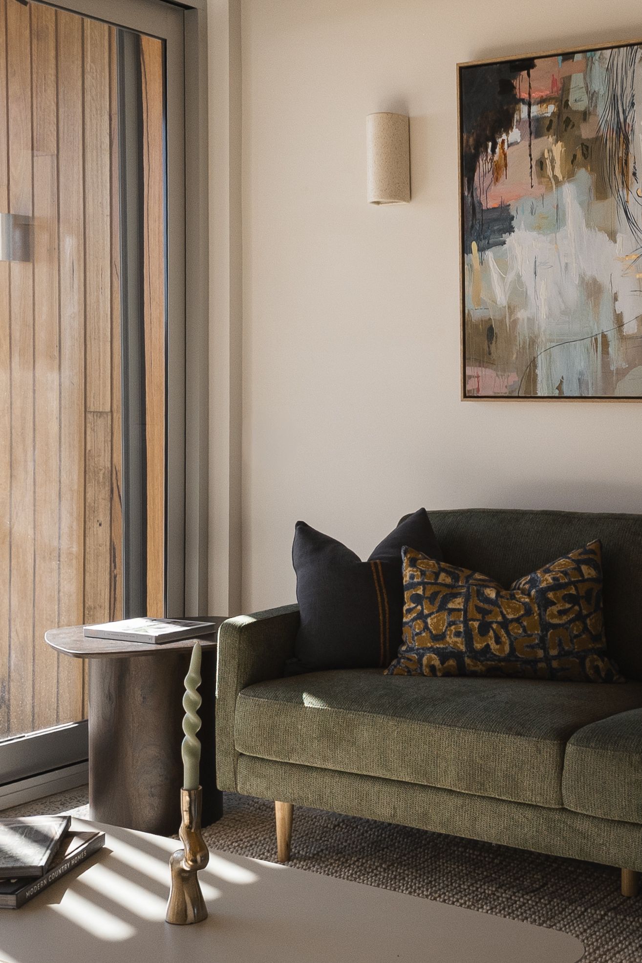 Green velvet sofa with print cushion, abstract wall art, sculptural side table, and warm sconce light in living room.
Middleton Fields
