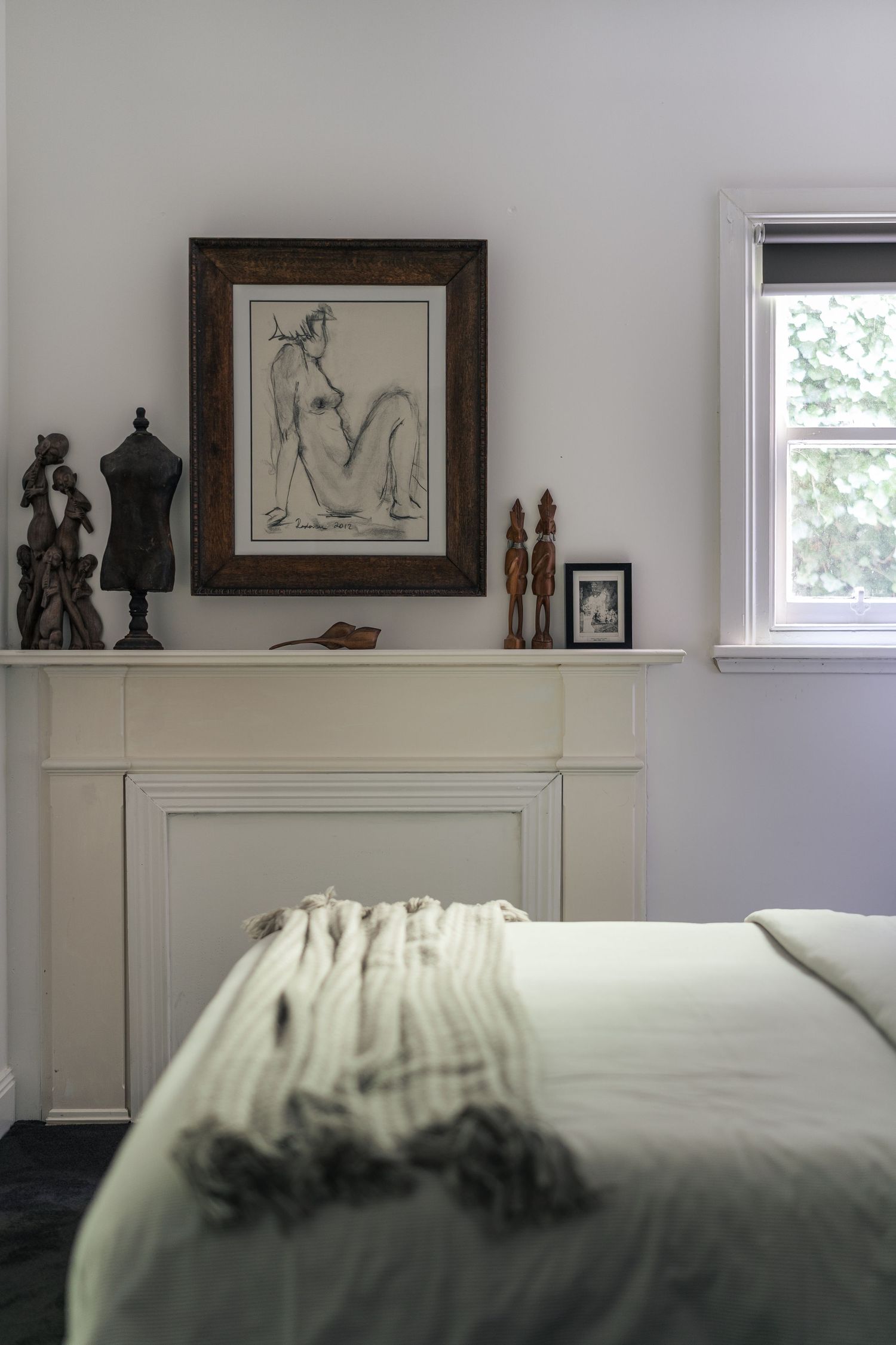 White bedroom with decorative fireplace mantel displaying framed artwork and wooden sculptures.

Piccadilly House