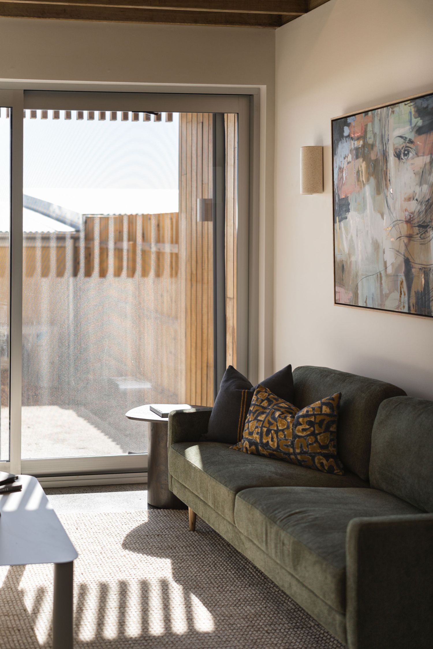Modern living room with green velvet sofa, decorative pillows, abstract wall art, and sliding glass door to wooden privacy fence.

Middleton