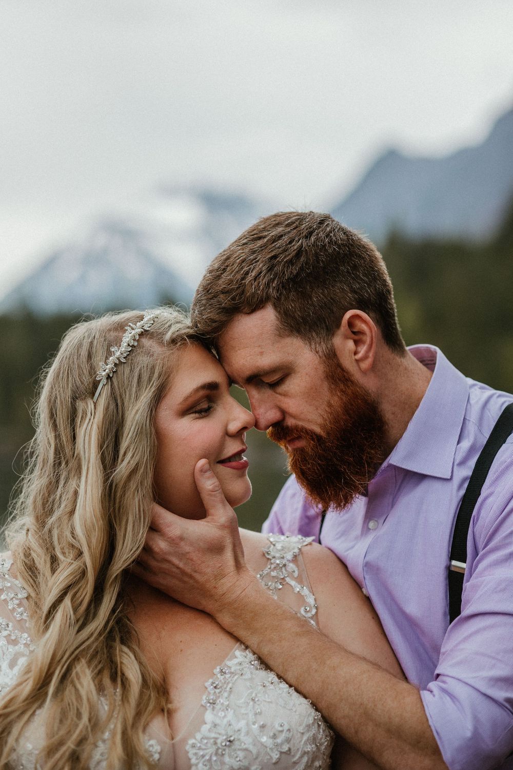 Bride and groom share an intimate forehead touch moment with misty mountain backdrop at outdoor wedding.