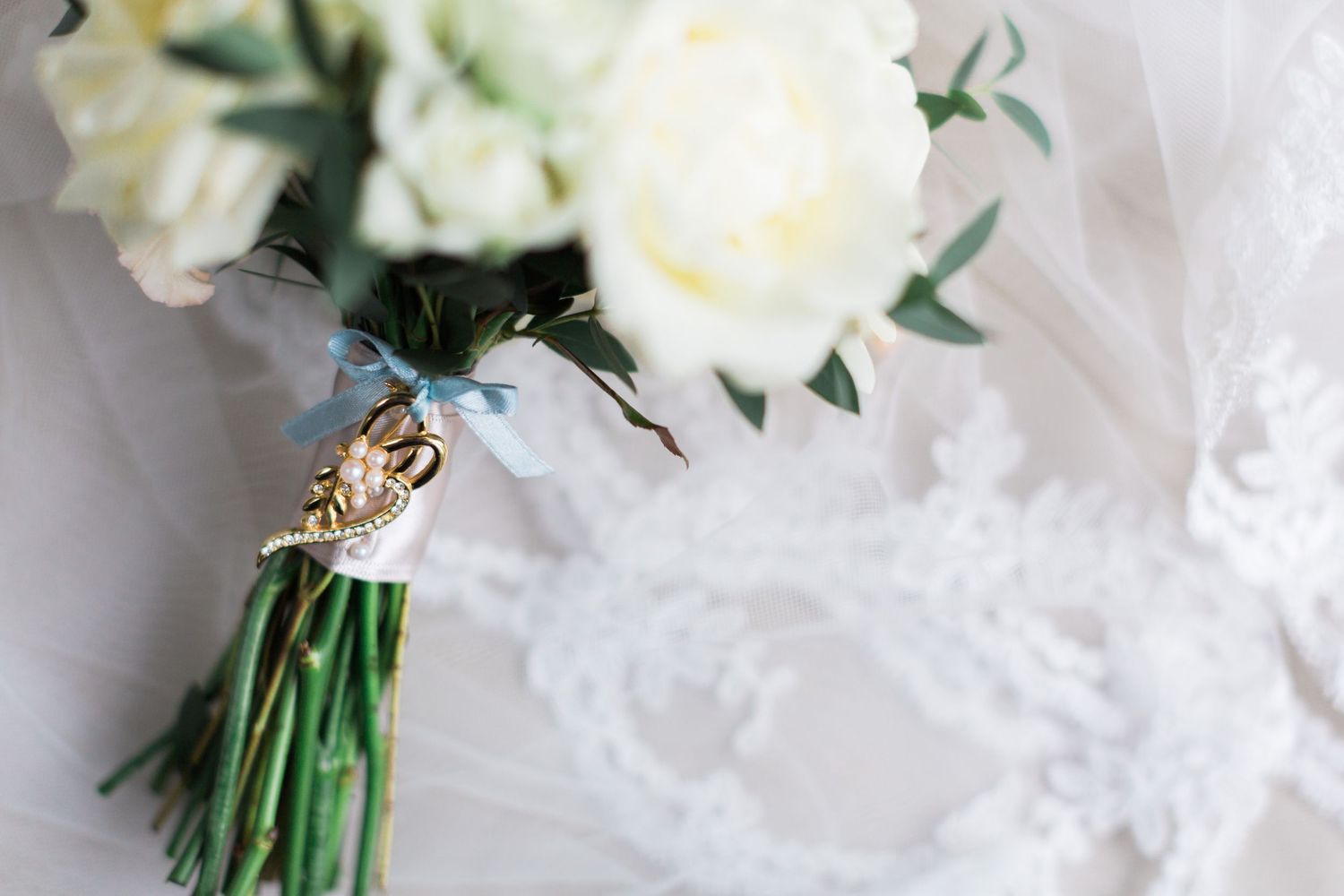 Elegant bridal bouquet of white roses with gold charm accent on lace veil background.