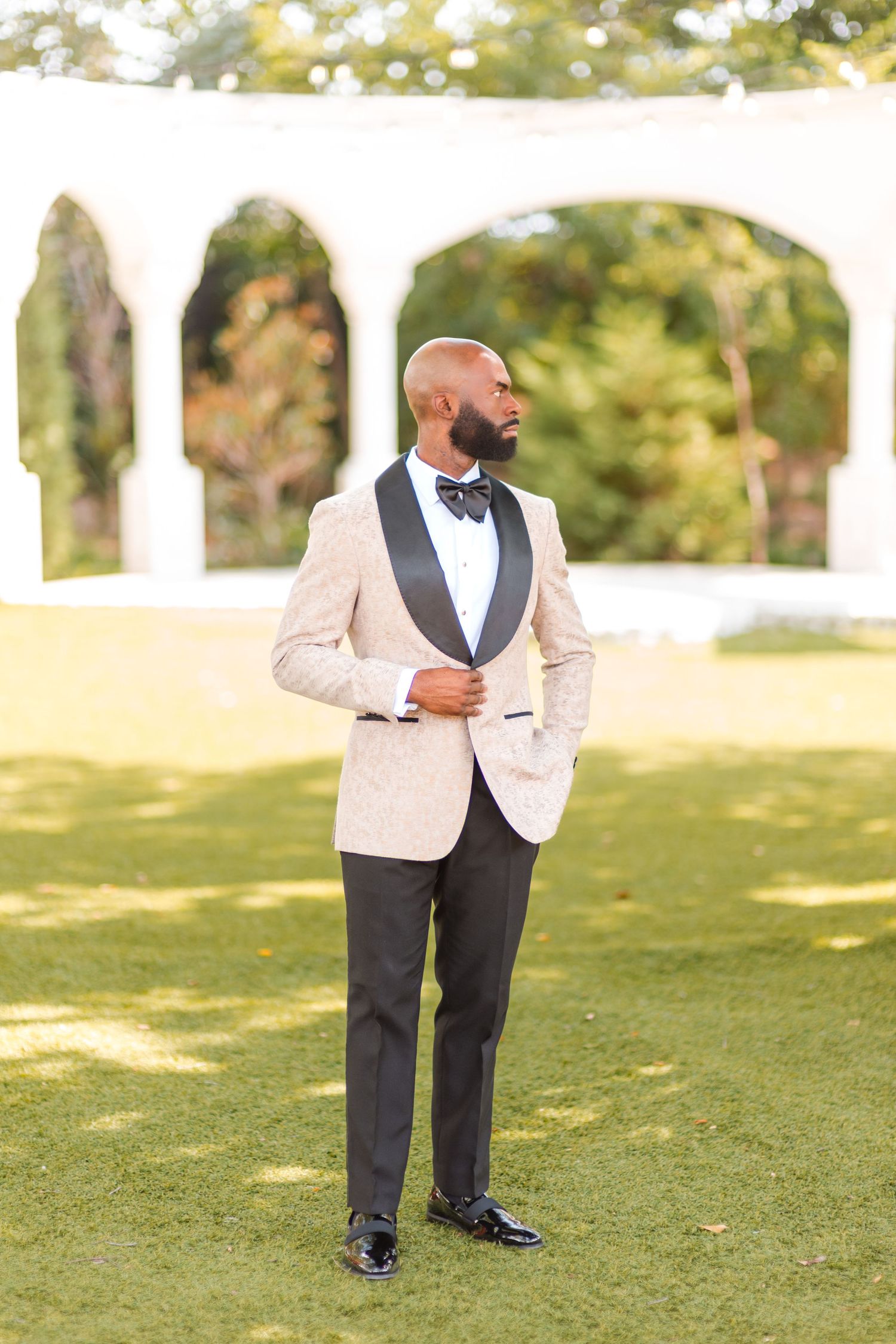 A person in a white dinner jacket and black pants stands on a lush green lawn during an outdoor event.